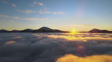 Ufuktaki Karpat dağlarının uzak karanlık zirveleriyle beyaz yoğun sis üzerinde canlı gün doğumunun havadan görüntüsü.