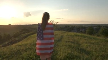 Gün batımında dışarıda Amerikan bayrağıyla poz veren mutlu genç kadın. Amerika 'nın bağımsızlık gününü kutlayan pozitif kız. Uluslararası Demokrasi Günü.