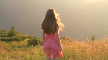 Kırmızılı genç kadın çimenli bir tarlada duruyor rüzgarlı bir sonbahar akşamında doğanın tadını çıkarıyor..