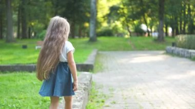 Güneşli bir günde yeşil bir yaz parkında açık havada yürüyen uzun saçlı güzel bir kızın arka görüntüsü..