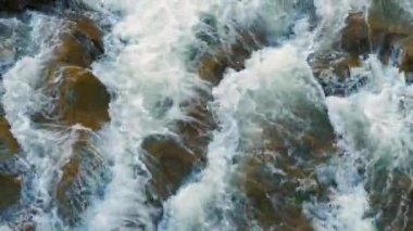 Nehir şelalesinin havadan görünüşü berrak turkuaz suyu kalın beyaz köpüklü ıslak kayaların arasına düşüyor..