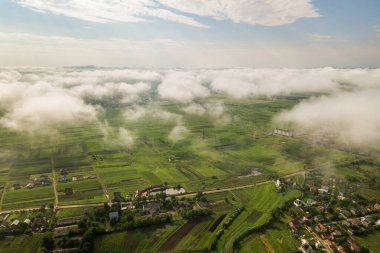 Yazın yeşil tarlalar arasında sıralı binalar ve kıvrımlı sokaklar olan bir kasaba ya da köyün üstündeki beyaz bulutların hava görüntüsü. Yukarıdan kırsal alan.