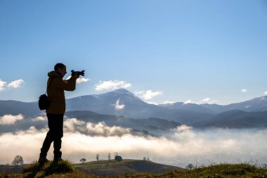 Sonbahar dağlarındaki sabah manzarasını çeken karanlık bir fotoğrafçının silüeti..