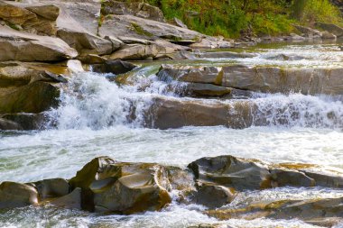 Küçük şelaleli dağ nehri berrak turkuaz suyla kalın beyaz köpüklü ıslak kayaların arasına düşüyor..