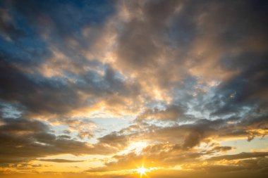 Turuncu batan güneş ve mavi gökyüzü tarafından aydınlatılan kabarık bulutlarla dramatik günbatımı manzarası.