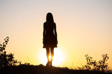 Yazın gün batımının tadını çıkaran bir taşın üzerinde duran genç bir kadının karanlık silueti..