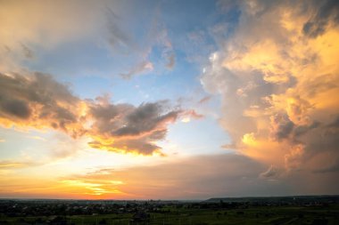 Turuncu batan güneş ve mavi gökyüzü tarafından aydınlatılan kabarık bulutlarla dramatik günbatımı kırsal manzarası.