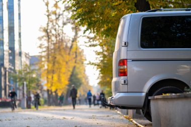 Yolcu minibüsü, sonbaharda bulanık yürüyen yayalarla şehir caddesi kenarına park edilmiş..