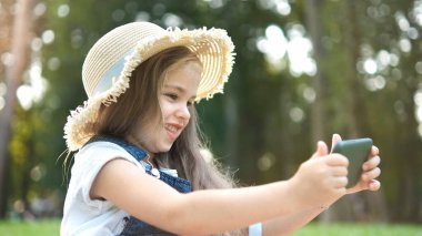 Mutlu gülümseyen kız yazın açık havada cep telefonuna bakıyor..