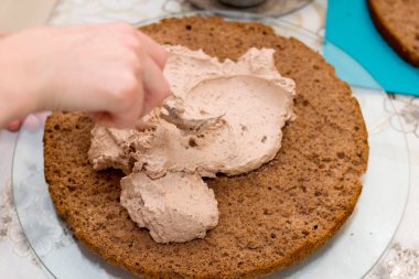 Evde kek pişirme süreci. Çikolatalı bisküvinin üzerine kadın el kreması dök. Mutfak ve lezzetli tatlı konsepti.