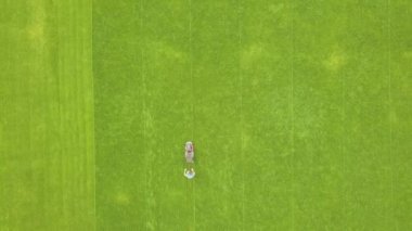 Yazın futbol sahasında çimenleri biçen ve çim biçen küçük işçi figürünün havadan görünüşü..