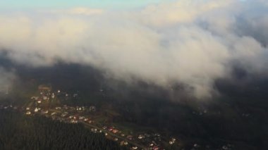 Gün batımında dağ tepelerini ve köy evlerini kaplayan karamsar sis bulutlarının hava manzarası.