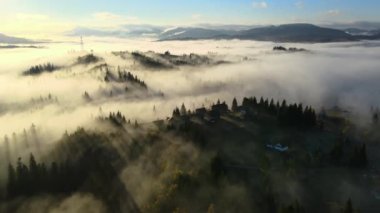 Güneşin doğuşuyla sisli dağlarda tepedeki küçük köy evlerinin hava manzarası..