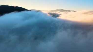 Güneşin doğuşuyla dumanlı dağ tepelerini kaplayan sisli ve hızlı bulutların üzerindeki hava manzarası.