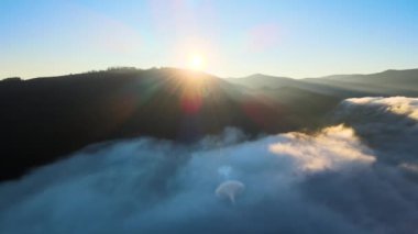 Sisli ve hızlı bulutların üzerindeki hava manzarası gün batımında dağ tepelerini kaplıyor..