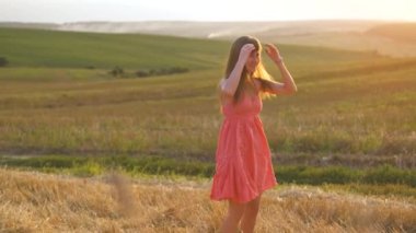 Mutlu, uzun saçlı genç kadın gün batımında altın buğday tarlasında dans ediyor..