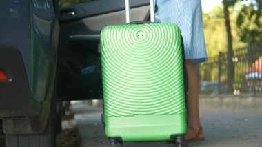 Genç kadın sürücü yeşil bavulu şehir caddesine koyuyor. Seyahat ve tatil kavramı.