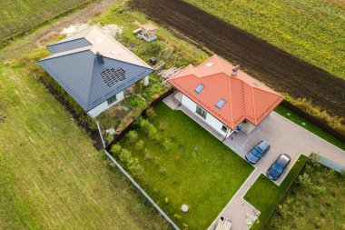 Çatı pencereleri ve yeşil çimenli asfalt avluda arabaları olan çatı kiremitli ev manzarası..