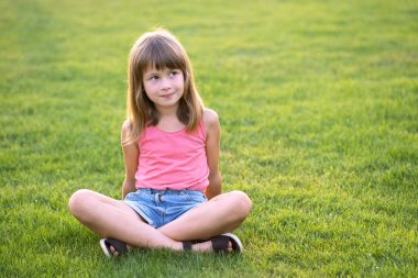 Genç mutlu kız sıcak yaz gününde yeşil çimlerde otururken dinleniyor.