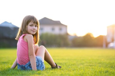 Genç mutlu kız sıcak yaz gününde yeşil çimlerde otururken dinleniyor.