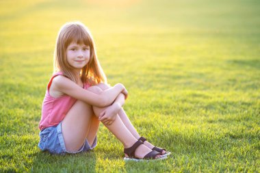 Genç mutlu kız sıcak yaz gününde yeşil çimlerde otururken dinleniyor.