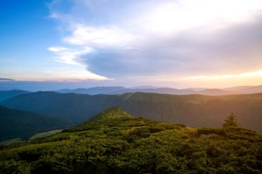 Yaz akşamı dağ manzarası çimenli tepeler ve renkli günbatımında uzak tepeler.