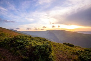 Yaz akşamı dağ manzarası çimenli tepeler ve renkli günbatımında uzak tepeler.