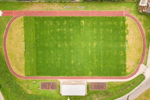 Aerial view of sports stadium with red running tracks and green grass football field.