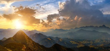 Yüksek tepeleri ve sisli vadisiyle gün batımı manzarası kayalık dağlarda canlı bir akşam gökyüzü altında.
