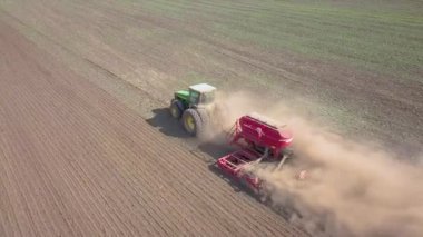 Yeşil traktörün havadan görünüşü, toprağı işlemesi ve kuru bir tarlayı tohumlaması. Çiftçi, ekili ekiciyle tarımsal çalışmaların ilkbahar başlarında tarım öncesi etkinliklerinin bir parçası olarak tarla hazırlıyor..