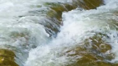 Berrak turkuaz suyu olan dağ nehri, kalın beyaz köpüklü ıslak kayaların arasına dökülüyor..