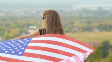 Genç, mutlu, uzun saçlı Amerikalı kadın rüzgârda sallanıyor. Amerikan bayrağı üzerinde. Açık havada dinleniyor, sıcak yaz gününün tadını çıkarıyor..
