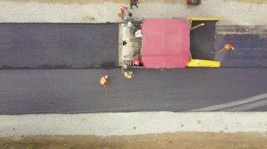 Çalışan işçiler ve asfalt döşeyen makinelerle yeni yol yapımının havadan görünüşü.