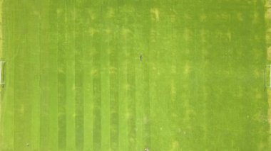Yazın futbol sahasında çimenleri biçen ve çim biçen küçük işçi figürünün havadan görünüşü..