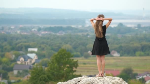 長い髪の若い女性で短い黒のドレス丘の上に立って暖かい夏の日を楽しむ — ストック動画
