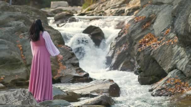 身穿长裤晚礼服的年轻漂亮女子站在小山小河边 流水湍急 — 图库视频影像