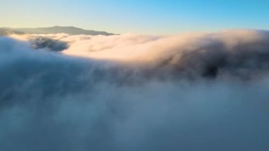 Sisli ve hızlı bulutların üzerindeki hava manzarası gün batımında dağ tepelerini kaplıyor..