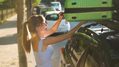 Genç kadın sürücü yeşil bavulu şehir caddesindeki çatı rafına koyuyor. Seyahat ve tatil kavramı.