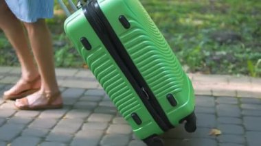 Genç bir kadının yaz günü yeşil bavuluyla şehir kaldırımında yürümesi. Seyahat ve tatil kavramı.