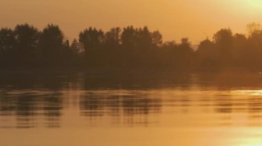 Göl suyunun parlak yüzeyi, parlak sarı günbatımını yansıtan dalgalarla..