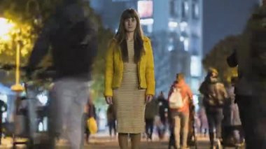 Gece vakti aydınlanmış şehir caddesinde tanınmayan insanların siluetlerini hareket ettiren genç bir kadının hızlandırılmış görüntüleri..
