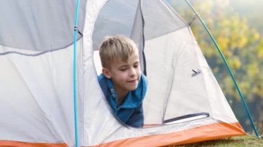 Yürüyüşçü çocuk dağ kampında bir çadırda oturmuş doğa manzarasının tadını çıkarıyor..