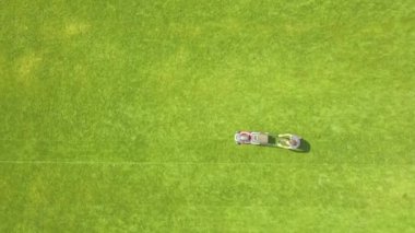 Yazın futbol sahasında çimenleri biçen ve çim biçen küçük işçi figürünün havadan görünüşü..