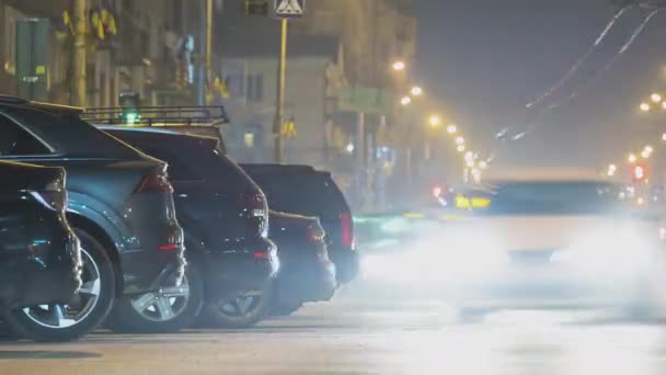 Крупный План Припаркованных Автомобилей Обочине Дороги Ночью Размытым Видом Светофоры — стоковое видео