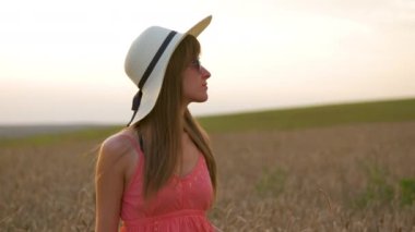 Mutlu, uzun saçlı genç kadın gün batımında altın buğday tarlasında yürüyor..