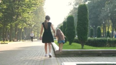 Anne ve uzun saçlı küçük kızı yaz parkında el ele yürüyorlar..