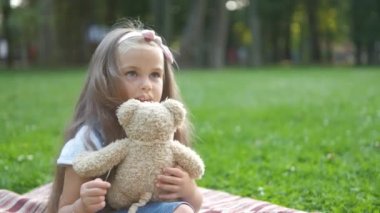 Mutlu çocuk oyuncak ayısıyla oynuyor yaz parkında yeşil çimlerde oturuyor.