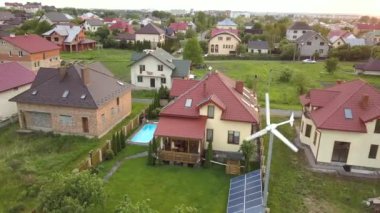 Banliyö evleri ve yeşil çimlerle kaplı özel ev çatıda güneş panelleri, mavi su ve rüzgar türbini jeneratörlü yüzme havuzu..