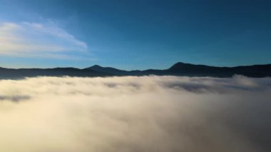 Sisli ve hızlı bulutların üzerindeki hava manzarası gün batımında dağ tepelerini kaplıyor..