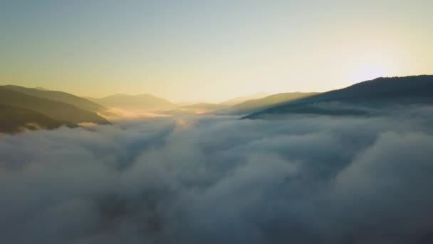 水平線上の山の丘の遠く暗いシルエットと白い濃い霧の上の鮮やかな日の出の空中ビュー — ストック動画